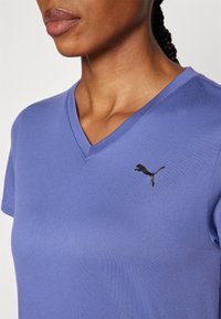 Lilla v-hals t-skjorte i glatt stoff med korte ermer og en svart Puma-logo på venstre bryst.