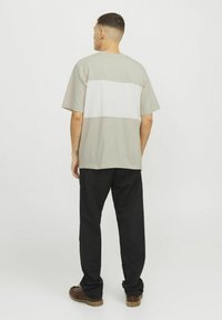Relaxed-fit t-shirt in light gray with a white horizontal stripe. Short sleeves, cotton material, and a round neck. Paired with black pants.