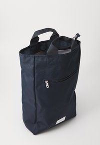 Granatowa torba tote wykonana z wytrzymałego materiału, z dwoma górnymi uchwytami, przednią kieszenią na zamek błyskawiczny i minimalistyczną białą metką.
