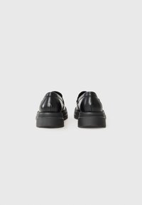 Scarpe in pelle nera con punta arrotondata, design a profilo basso e suola in gomma testurizzata. La vista posteriore mette in mostra la tomaia liscia e il dettaglio delle cuciture.