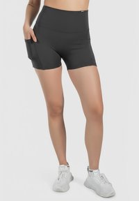 Shorts sportivi neri a vita alta realizzati in tessuto elastico, con tasche laterali e un design aderente e liscio. Abbinati a scarpe sportive bianche.