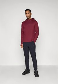 Vinröd långärmad huva tröja kombinerad med svarta sportbyxor. Tyget är slätt, med subtila logodetaljer på tröjan och byxorna.