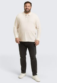 Langarm-Polohemd in Creme, mit einer Dreiknopf-Leiste, geripptem Material und Slim-Fit, kombiniert mit dunklen Jeans und weißen Sneakern.