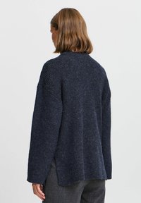 Pull en tricot côtelé bleu marine foncé avec des manches longues, un col haut et des fentes sur les côtés. Texture douce avec un design décontracté et détendu.