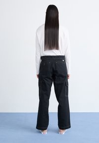 Black cargo pants with a loose fit, featuring multiple pockets, yellow stitching, and a subtle logo on the back waistband.