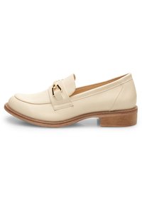 Mocassino in pelle beige con punta arrotondata e accentuazione decorativa in oro. Presenta un tacco in legno basso e una suola piatta. Texture liscia in tutto il prodotto.