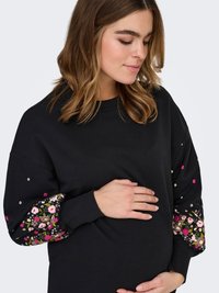 Black sweatshirt featuring floral embroidered accents on the sleeves, complemented by small decorative embellishments. Soft fabric, relaxed fit.