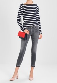 Granatowa i biała w paski bluzka z długim rękawem, szare dopasowane dżinsy, różowe buty na obcasie w klocku oraz mała czerwona i niebieska torebka na ramię.