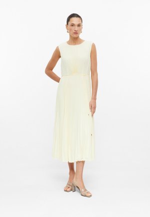 Frau trägt ein ärmelloses, plissiertes Elfenbein-Midikleid mit tailliertem Schnitt, beige Absatzsandalen und goldene Creolen vor weißem Hintergrund.