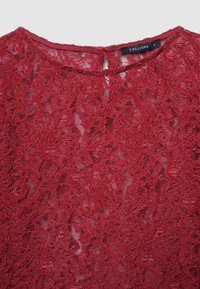 Top in pizzo rosso con scollatura rotonda e dettaglio a chiave sulla schiena. Presenta motivi floreali e una superficie texturizzata. Etichetta del marchio visibile sul collo.