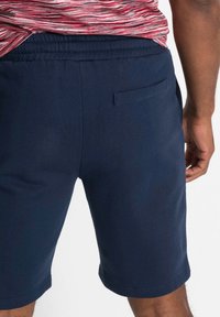 Pantaloni corti blu navy con cintura elastica, texture morbida e tasca posteriore a toppa. Il design presenta una silhouette pulita e semplice.