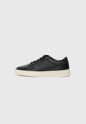 Baskets en cuir noires à tiges basses avec lacets noirs et semelle ivoire, présentées en profil latéral sur fond blanc.