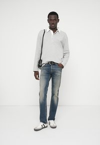Polo de manga longa cinza-claro com colarinho branco, combinado com jeans de ganga azuis e ténis brancos com detalhes pretos. Conjunto simples e casual.