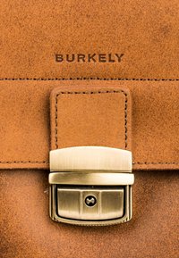 Borsa in pelle marrone con finitura testurizzata, dotata di una chiusura in metallo tono oro e logo impresso "BURKELY" sul davanti.