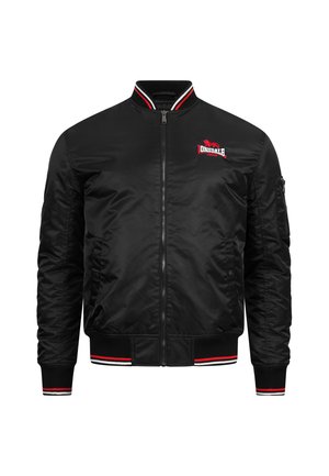 Musta pommikauppuasu satiinista punaisilla ja valkoisilla raidoilla kauluksessa ja hihoissa, jossa on logo rinnassa ja sivutaskut.