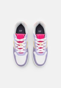 Zapatillas blancas con acentos en púrpura, rosa y amarillo, que presentan una superficie texturizada, cordones en contraste y la marca "GAP" en la lengüeta.