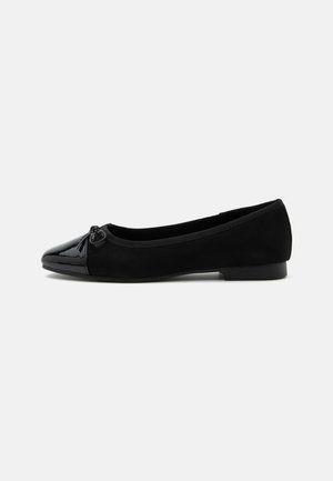 Ballerine noire avec bout en cuir verni, petit détail nœud et talon bas sur fond blanc uni.