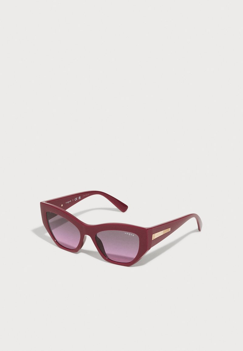 Óculos de sol burgundy com um design geométrico de olho de gato, lentes roxas degradê e detalhe em tom de ouro na haste. Feitos de plástico.