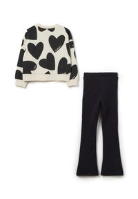 L'ensemble comprend un sweat-shirt court couleur crème avec de grands motifs de cœur noir et un legging noir évasé assorti, tous deux en tissu doux.