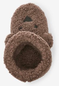 Chausson en peluche marron fait de tissu texturé avec une ouverture ronde. Doté d'un design de visage simple et d'une doublure intérieure douce.