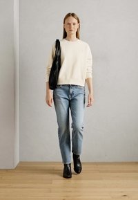 Sweatshirt crème avec des poignets côtelés, jeans droits bleu clair, et bottines noires; portant un sac en bandoulière noir texturé.