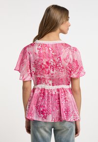 Blusa rosa a fantasia con tessuto trasparente, maniche corte a soffietto, scollatura con pizzo e orlo a peplo. La vista posteriore mostra un design intricato.