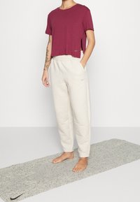 Camiseta burdeos de corte ajustado con mangas cortas, combinada con pantalones de chándal crema de textura, que presentan un logo sutil en el lado izquierdo.