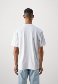 Tricou alb din bumbac, cu mâneci scurte și gât rotund, prezentat din spate, având un design simplu și croială relaxată.
