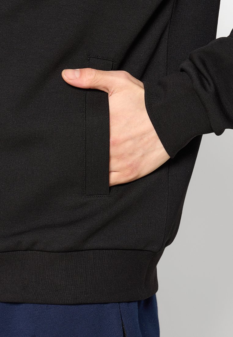 Schwarzer Sweatshirt mit Seitentasche, gerippten Bündchen und Saum. Der Stoff wirkt strukturiert und weich, mit einer taillierten Passform.