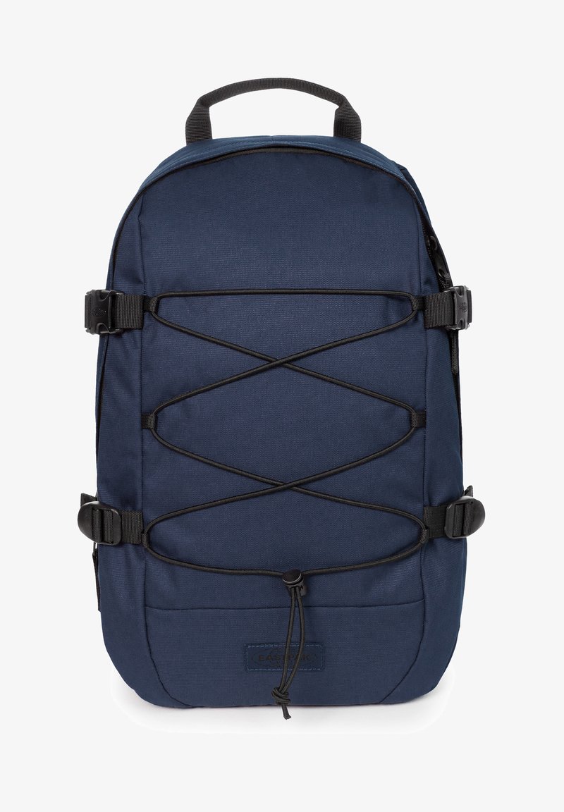 Mochila azul marino con un tejido texturizado, que presenta un sistema de cordones en la parte frontal, dos hebillas laterales y una asa superior para llevar.