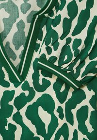 Tessuto a fantasia verde e crema con scollo a V e maniche arricciate, caratterizzato da un trim verde a contrasto e strisce orizzontali.