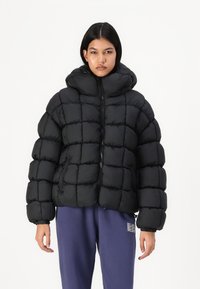 Svart puffjakke med hette, med et kviltet mønster, frontglidelås og elastiske mansjetter, sammen med løse blå joggebukser.