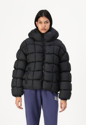 Svart puffjakke med hette, med et kviltet mønster, frontglidelås og elastiske mansjetter, sammen med løse blå joggebukser.