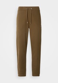 Braune Sweatpants mit einem Kordelzugbund, schmal zulaufendem Bein und Seitentasche. Weiche Textur und minimale Markenkennzeichnung am Bein.