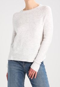 Maglione grigio chiaro in tessuto morbido, con colletto a girocollo, polsini a coste e una vestibilità rilassata con una texture sottile. Abbinato a jeans blu.