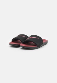 Chanclas negras con una correa gruesa y una plantilla texturizada en rojo, con un diseño ondulado. Suela de goma para agarre y durabilidad.