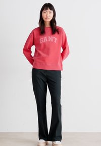 Czerwona bluza z kapturem z logo "GANT", w zestawie z czarnymi spodniami i białymi trampkami. Casualowy fason, prosty design i gładka tekstura.