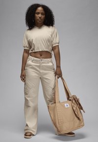 Top beige corto con maniche a sbuffo, abbinato a pantaloni cargo beige larghi. Porta una borsa a tracolla color tan con un logo e dettagli di sciarpa a fantasia.