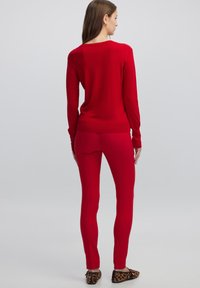 Maglione rosso a maniche lunghe in lana e leggings rossi attillati. L'outfit presenta un design semplice con una consistenza morbida e senza motivi visibili.