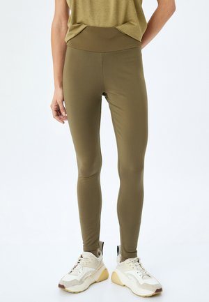 Olijfgroene leggings gemaakt van rekbaar materiaal, met een hoge tailleband en een aansluitend ontwerp. Gecombineerd met witte en beige sneakers.