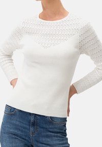 Top bianco a maniche lunghe con righe, caratterizzato da un motivo in pizzo testurizzato sulle spalle, scollo a barca e design aderente. Abbinato a jeans blu.