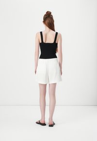 Top a canottiera nera a costine con spalline larghe abbinato a pantaloni corti di lino bianchi. L'outfit presenta un taglio casual e una vestibilità rilassata, completato da sandali neri.
