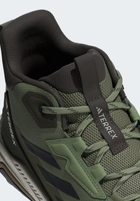 Groene textiel buitenschoen met een zwarte mesh kraag, versterkte veterogen, rubberen buitenzool en een opvallend logo aan de zijkant.