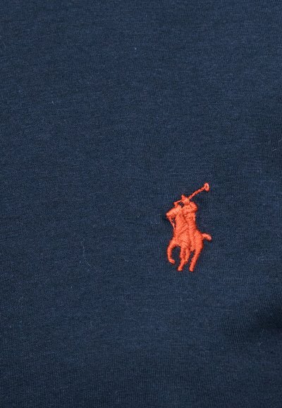 Czerwony, haftowany zawodnik polo z uniesionym młotkiem na ciemnoniebieskim tle tkaniny.
