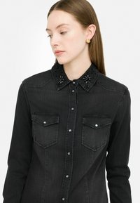 Camicia in denim nero con dettagli di collare in perline, due tasche sul petto e chiusura con bottoni frontali, caratterizzata da una vestibilità slim e una texture liscia.