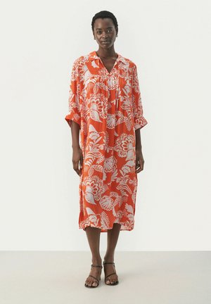 Vestido ligero y fluido en un brillante color naranja con patrones florales blancos. Presenta un cuello, mangas cortas y un corte a media altura. Tejido texturizado.