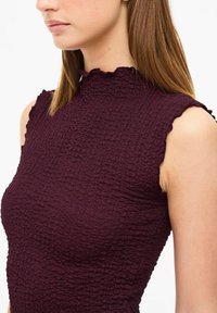 Vinet rödlös topp med hög, volangkrage och textil med en rynkad struktur. Tät passform.