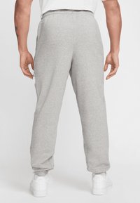 Grå bomulds-sweatpants med elastisk talje, tapered manchetter og sidelommer, båret med hvide sneakers.