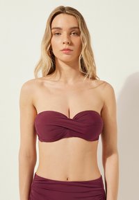 Haut de bikini bandeau Bordeaux avec détail torsadé, fabriqué à partir d'un tissu lisse. Le design présente des accents froncés et pas de bretelles.