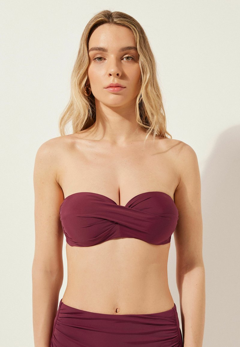Haut de bikini bandeau Bordeaux avec détail torsadé, fabriqué à partir d'un tissu lisse. Le design présente des accents froncés et pas de bretelles.